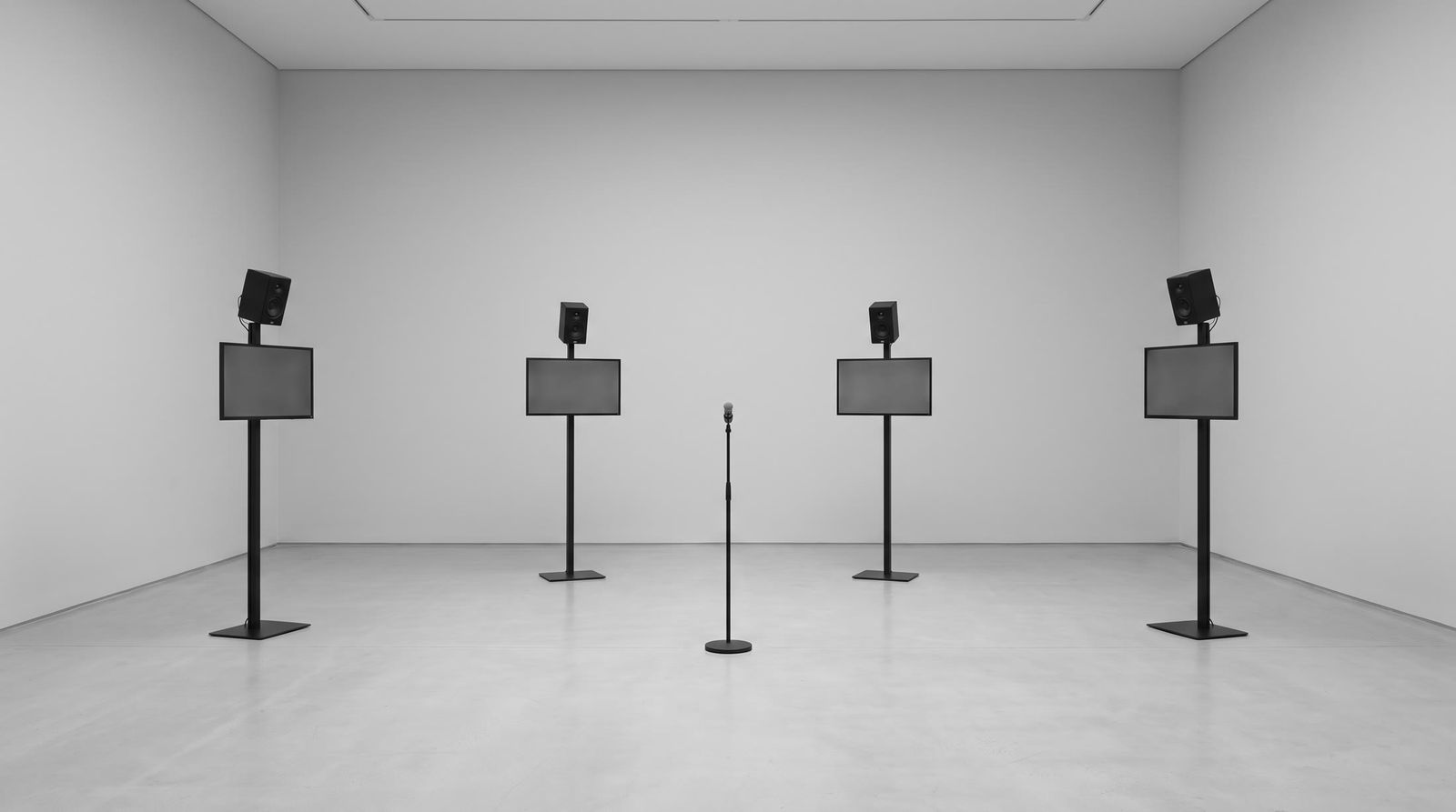 Installation mockup: four small screens on stands and near-field speakers in a white room.